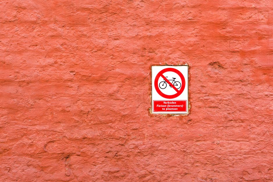 Close-up image of a weathered metal sign attached to a metal post, with peeling paint and rust. The sign reads 'THIS SPACE RESERVED 24 HOURS' in white capital letters on a black and brown background, indicating restricted parking or entry. The background features a white wall with visible peeling paint and minor cracks, typical of an exterior urban environment. This setting reflects conditions often encountered during house removals or moving logistics, where parking restrictions and waste rules can impact a home relocation process. Man with Van Heston provides removals services including loading and furniture transport, often requiring careful adherence to local regulations such as those indicated by parking restriction signs.